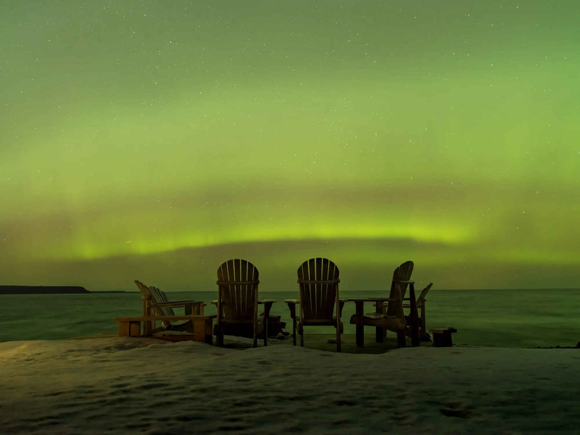 Green northern lights over a row of Muskoka chairs at Red Bay