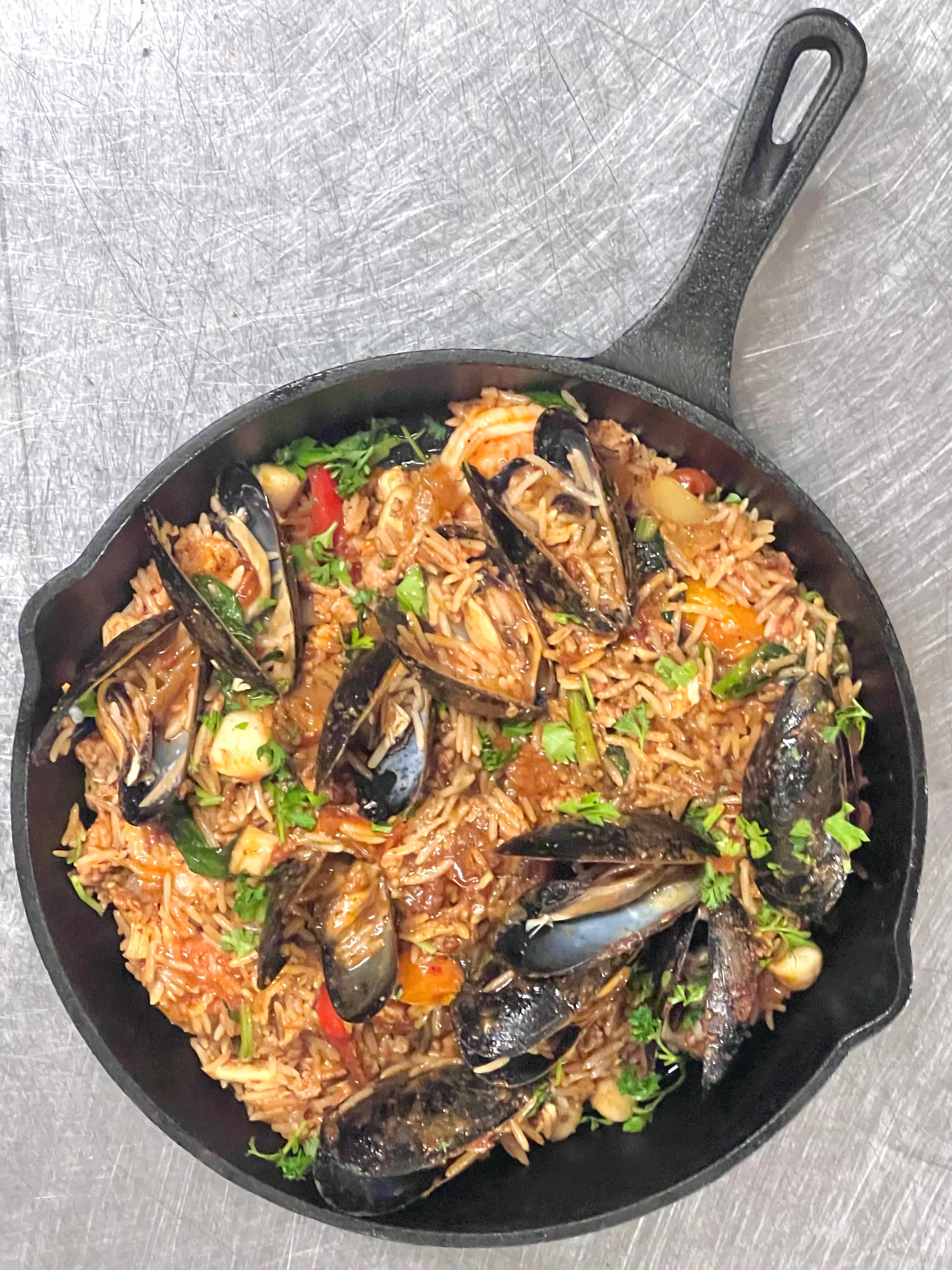A cast-iron skillet of mussels, rice and vegetables with fresh parsley