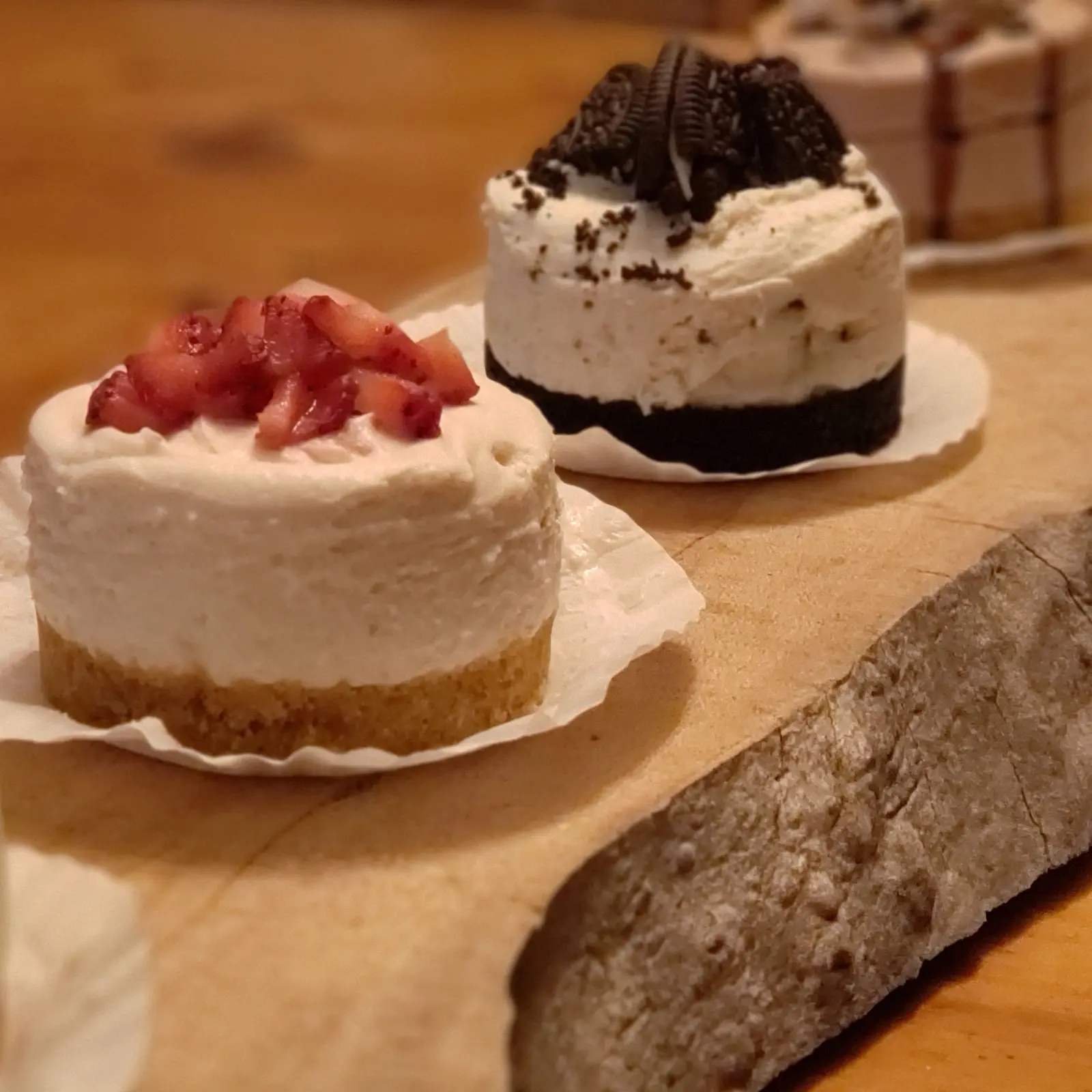 Two small cheesecakes, one with strawberries and one with chocolate cookie crumbs, on a wooden board