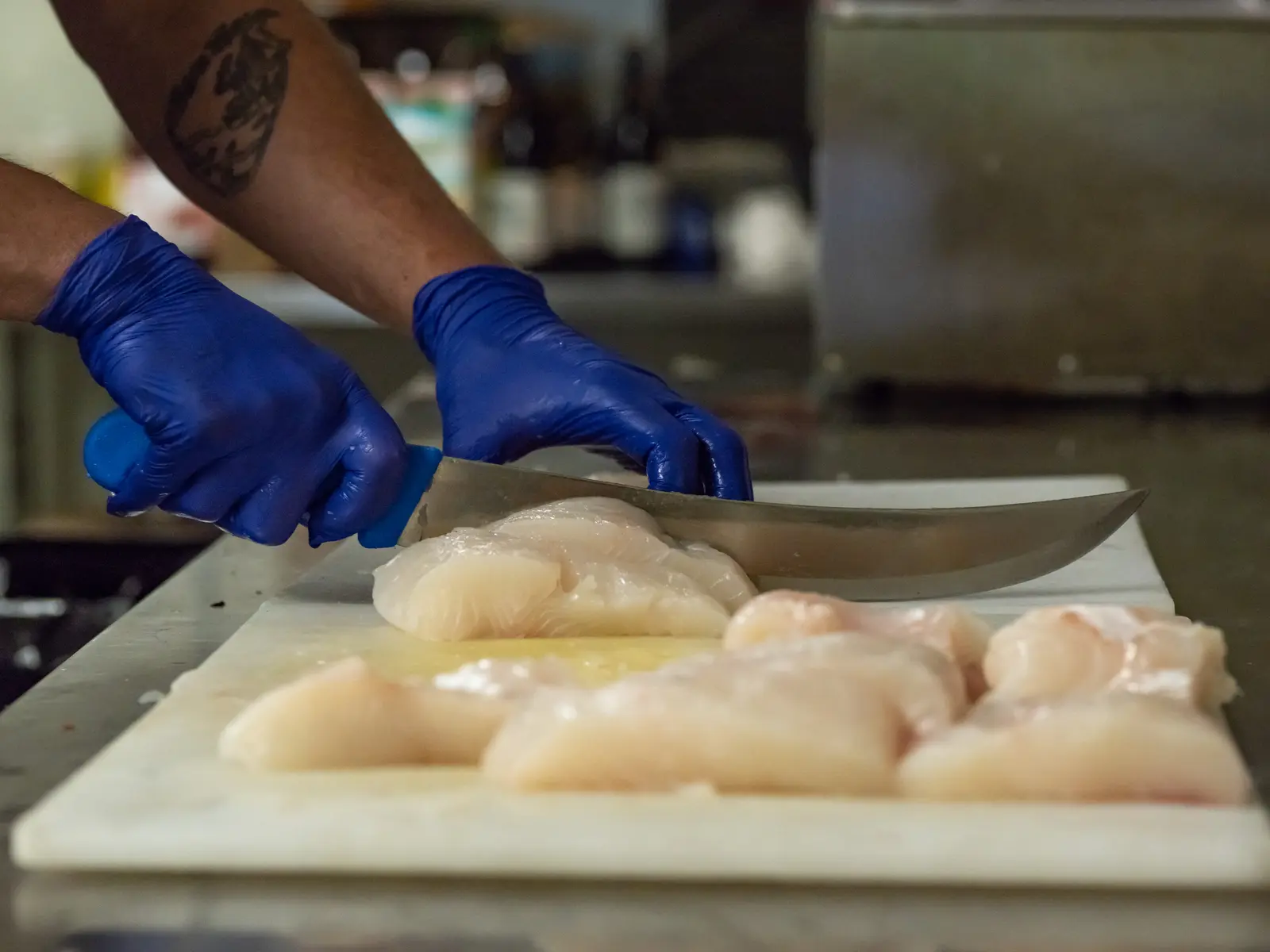 A cook in blue gloves cutting fish into portions in the lodge kitchen