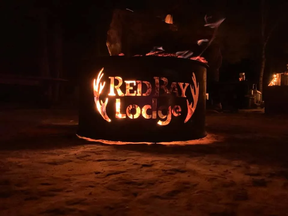 A steel fire pit with the Red Bay Lodge name cut out, glowing at night