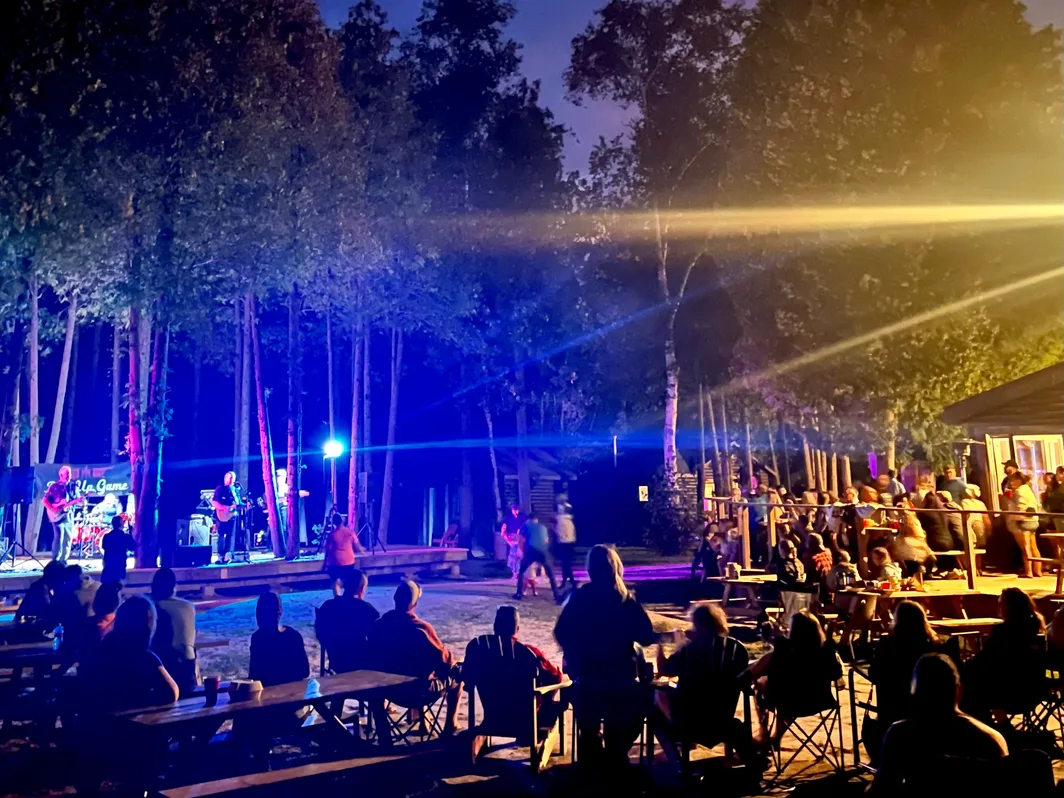 Guests at tables under blue stage lights at an evening show in the woods