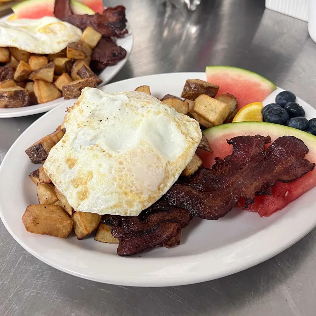 Breakfast plate of fried egg, bacon, home fries, watermelon and blueberries