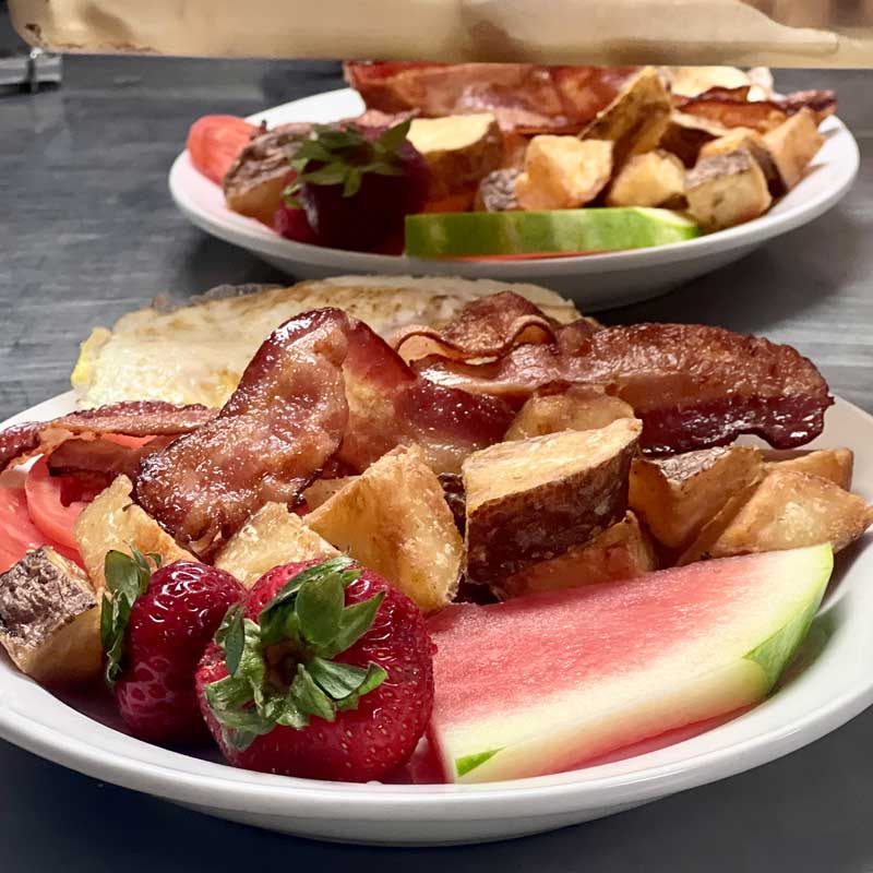 Two hot breakfast plates with eggs, bacon, home fries and fresh fruit