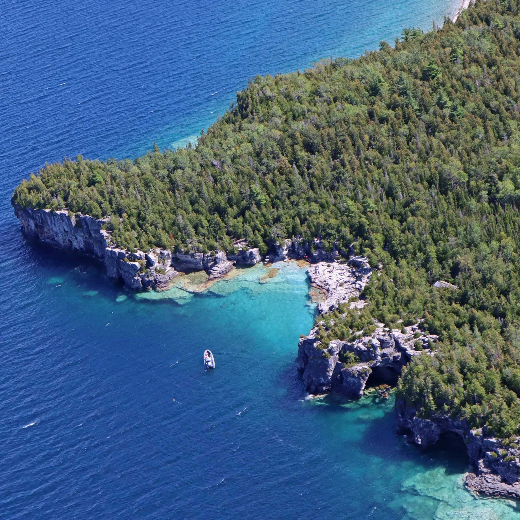 Aerial view of the rocky, forested Georgian Bay shoreline of Bruce Peninsula National Park with a small boat in the turquoise cove
