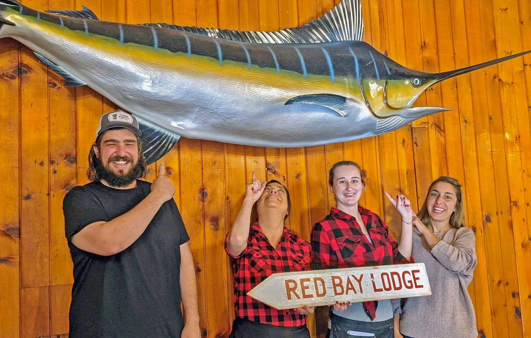 Four Red Bay Lodge staff pointing up at a mounted marlin, one holding a Red Bay Lodge sign