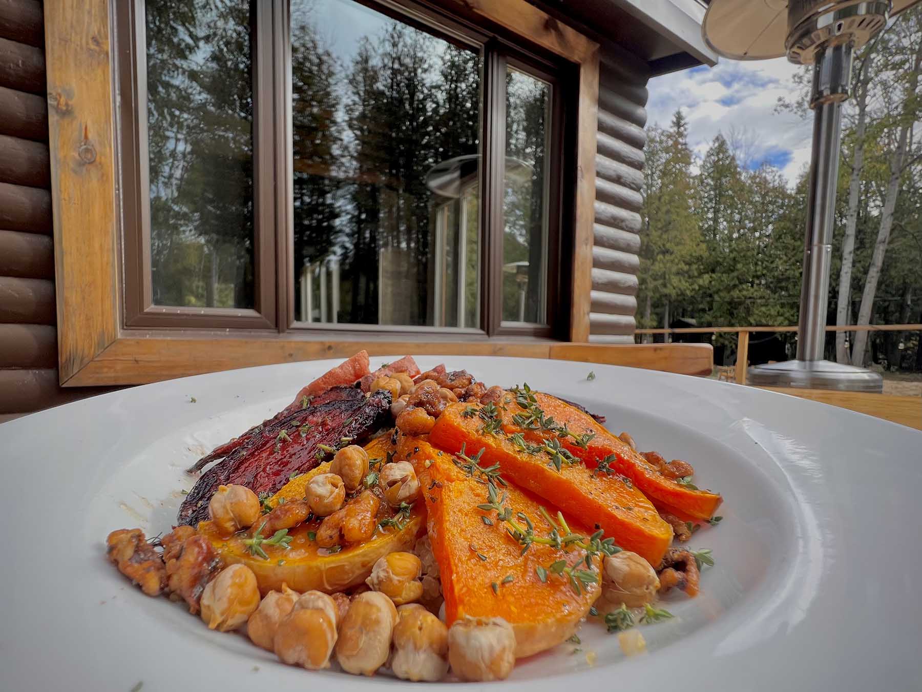 A plated dinner of roasted vegetables on a white plate beside a window at the lodge