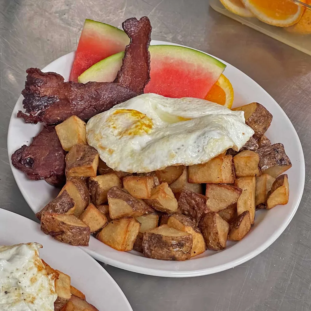 Breakfast plate with an egg, bacon, home fries and watermelon