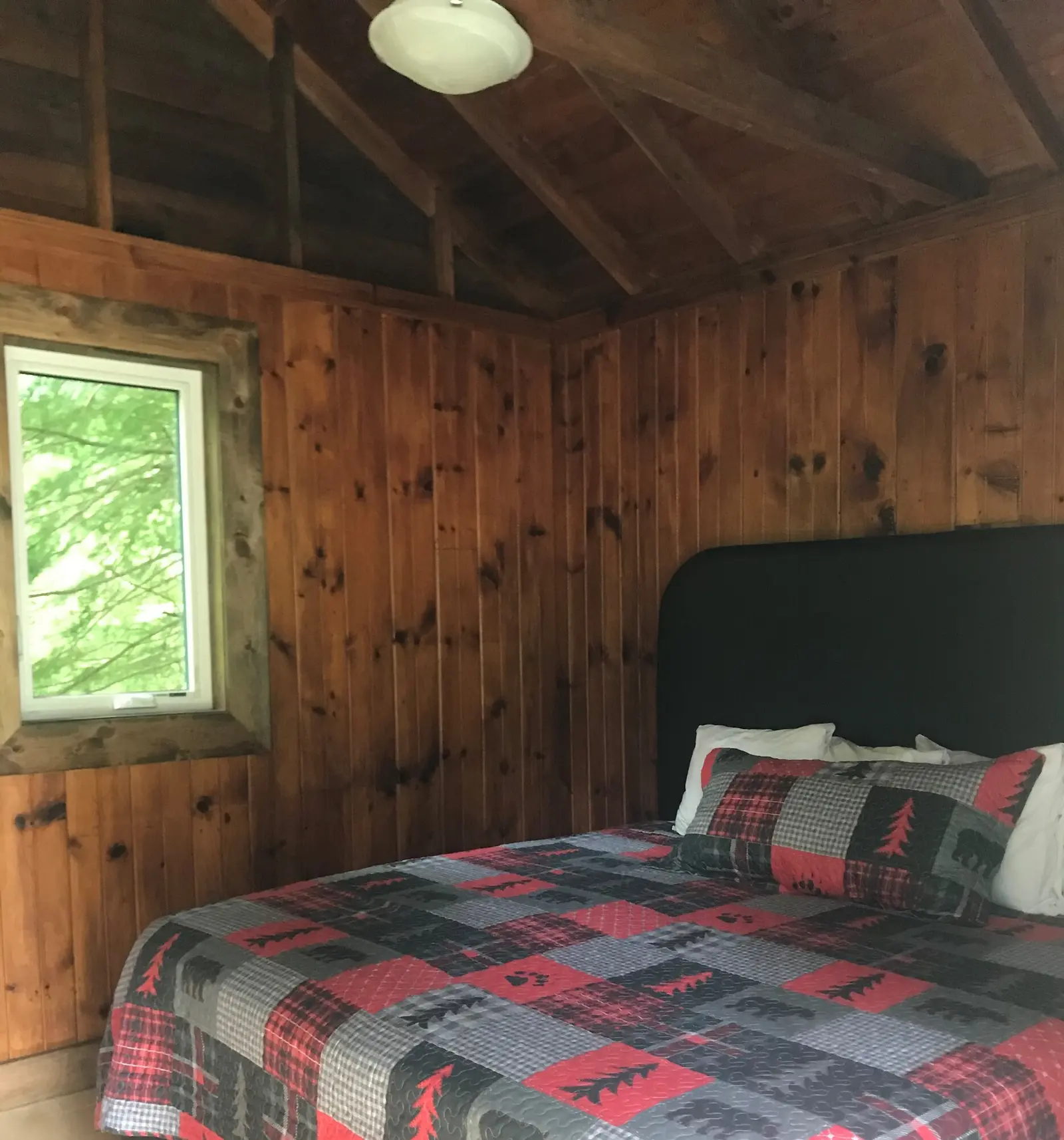 A queen bed with a red and black plaid quilt in the pine-panelled Birch