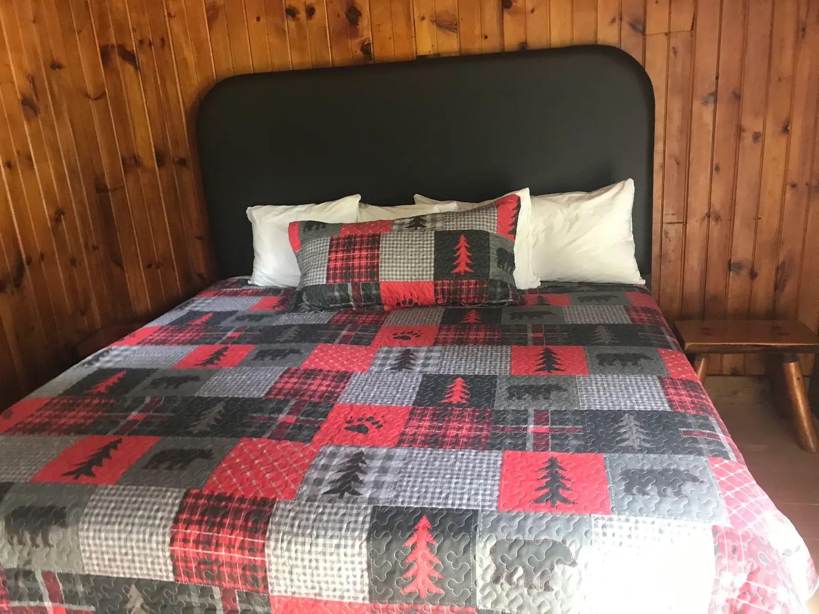 A queen bed with a plaid quilt inside the Birch, a 1 bedroom cabin