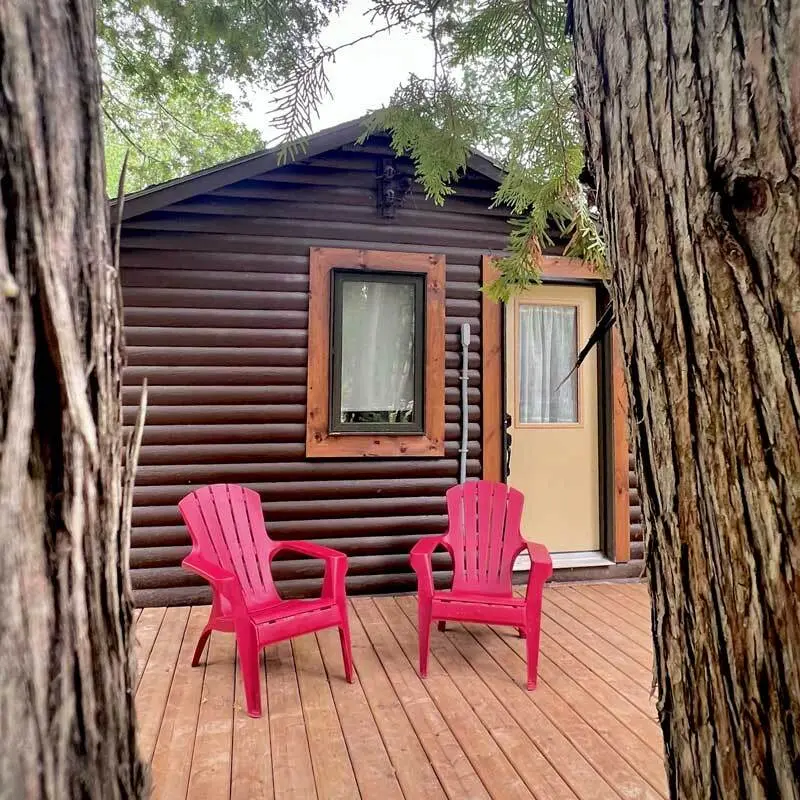 The Elm, a 1 bedroom cabin, with red chairs on the deck beside tall cedars
