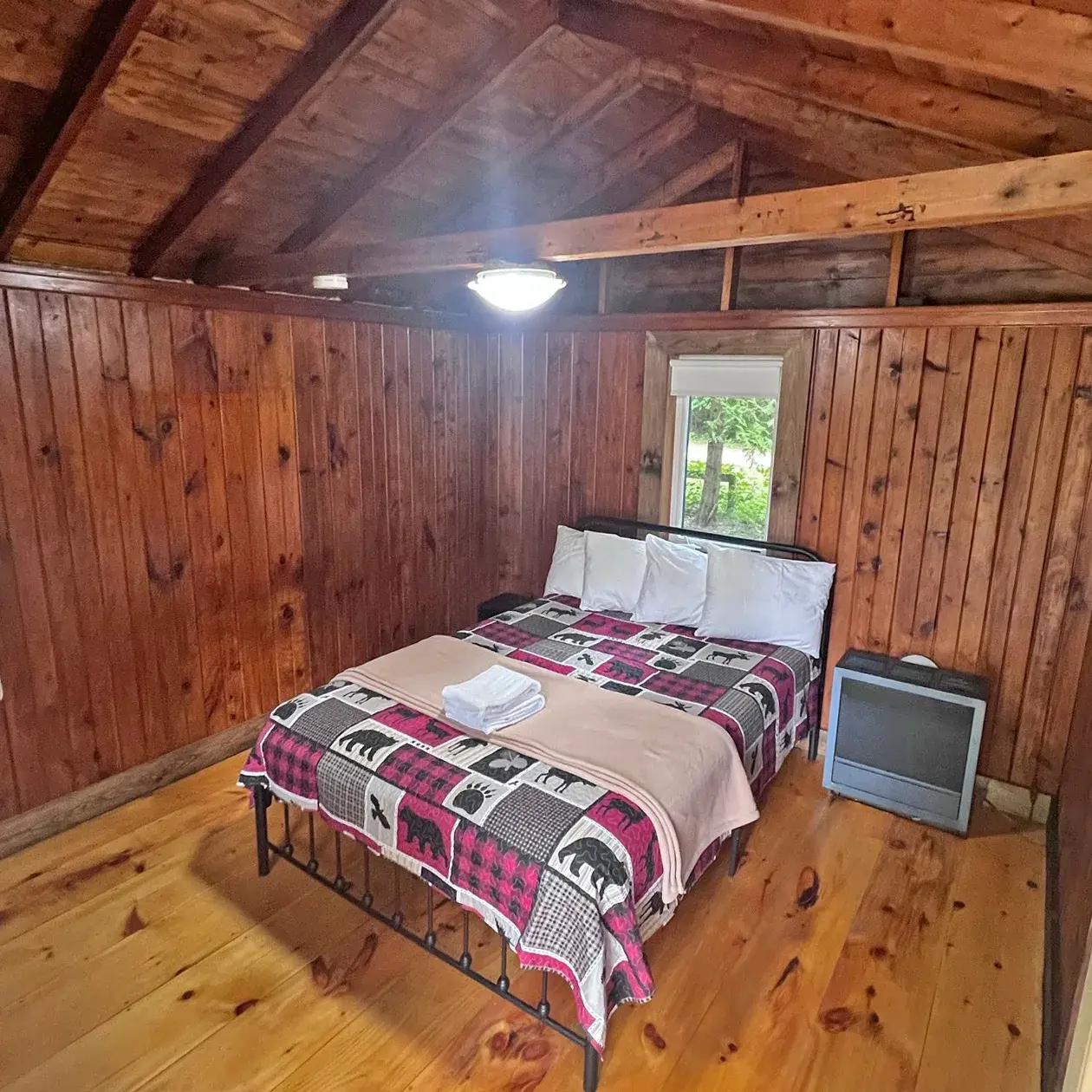 A bed with a plaid quilt under a window in a 1+ bedroom cabin