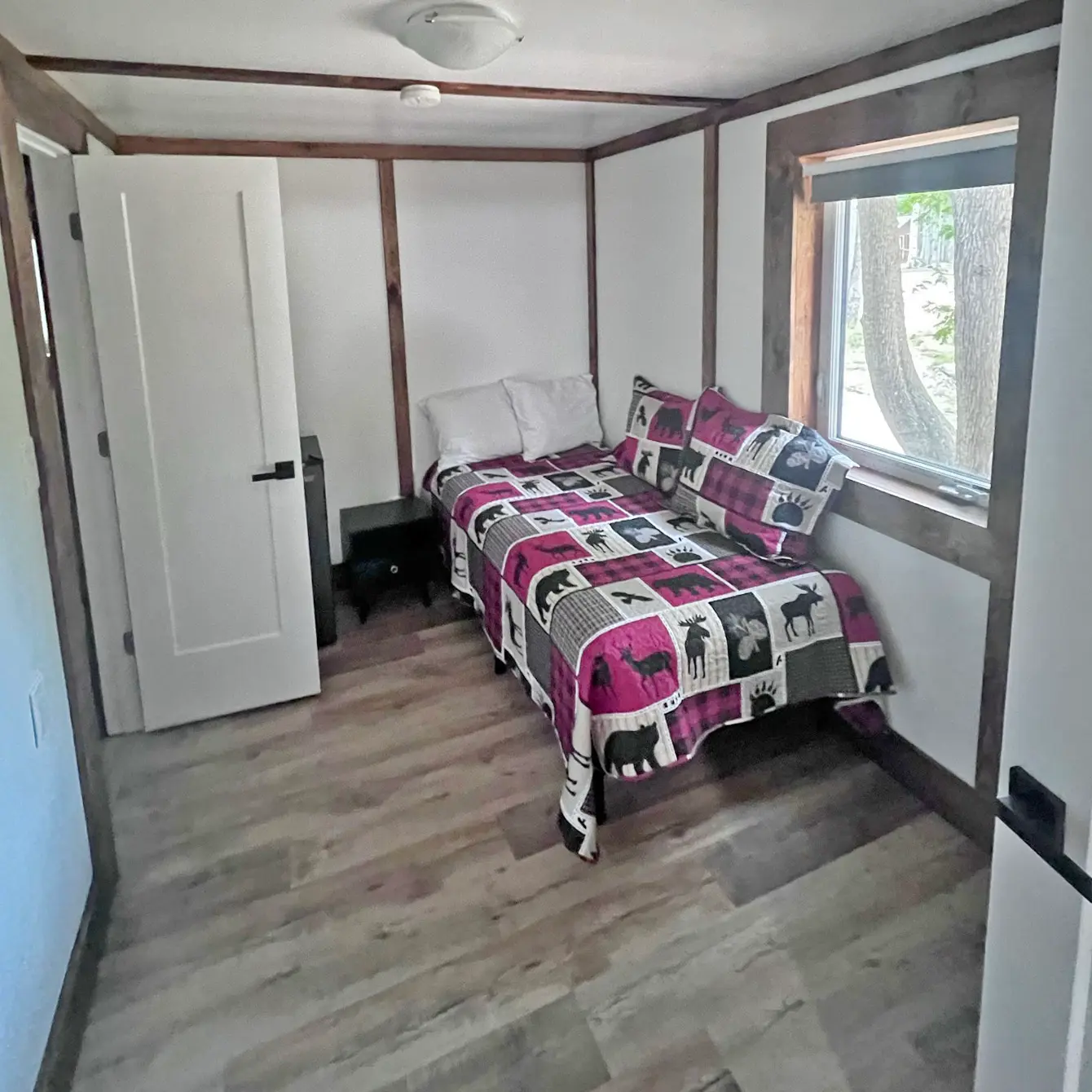 A bed under a bright window inside the Tamarack, a 1+ bedroom cabin