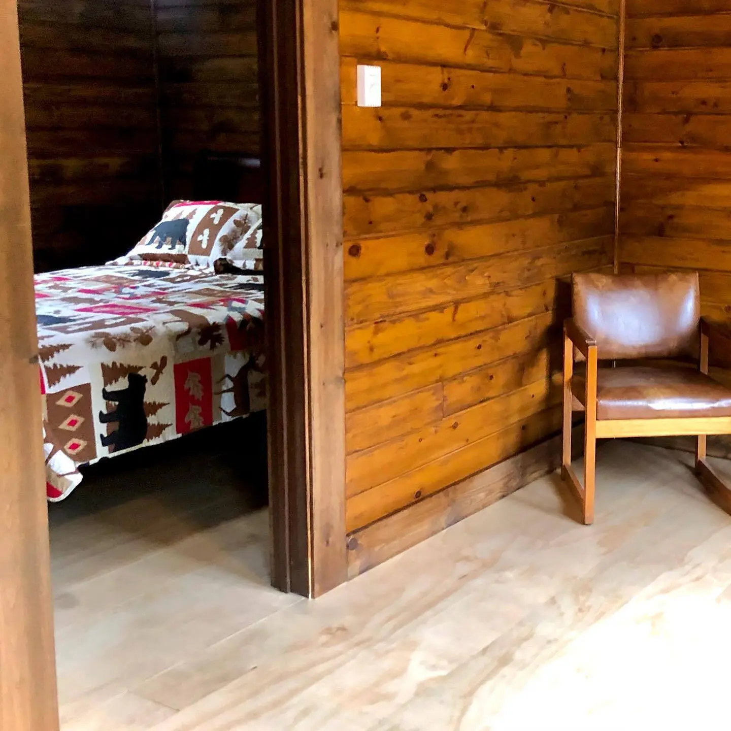 A leather chair beside a bed in a pine-panelled bedroom of the Red Cedar