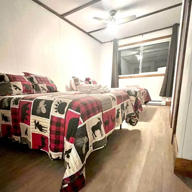 Two beds with plaid quilts and a ceiling fan in a lodge room