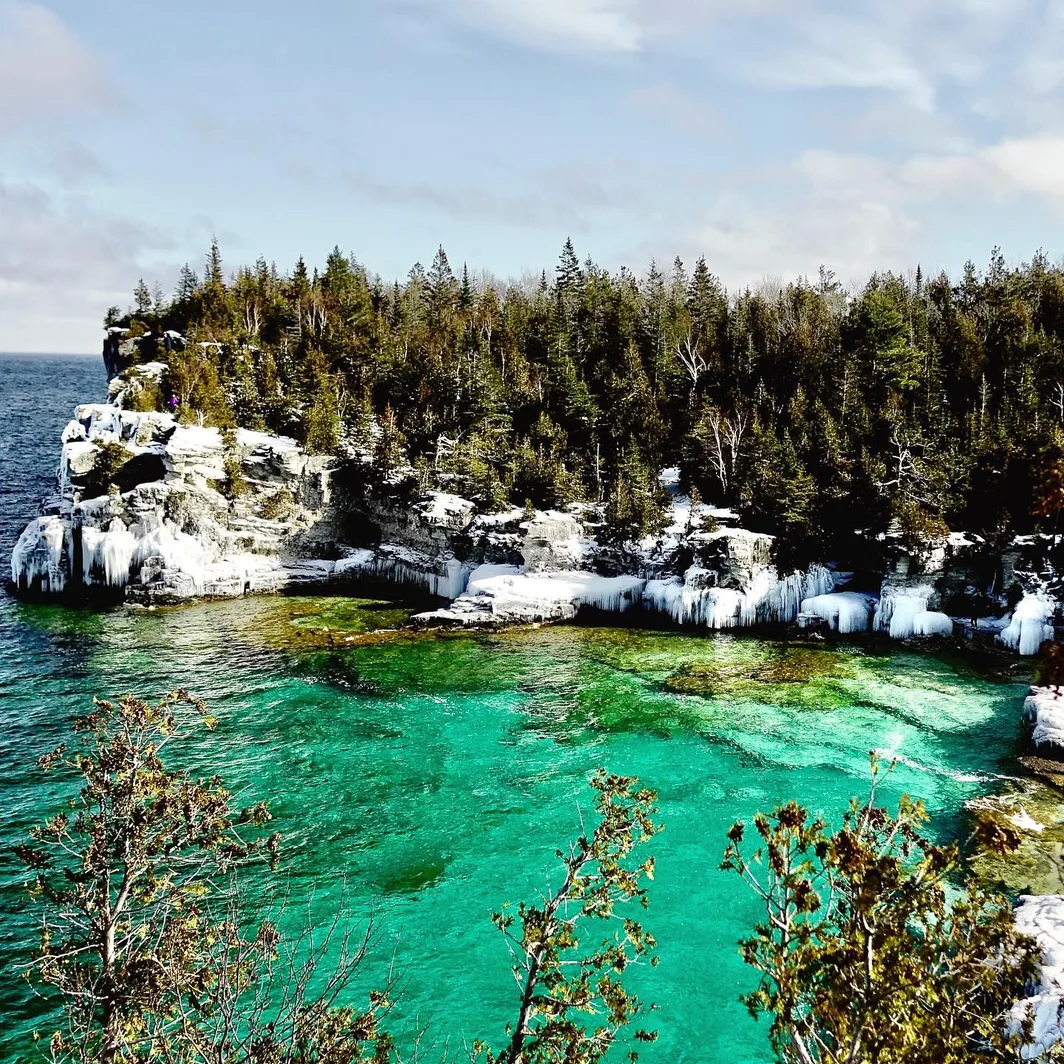 A rocky Georgian Bay shoreline with ice along the cliffs and clear turquoise water below