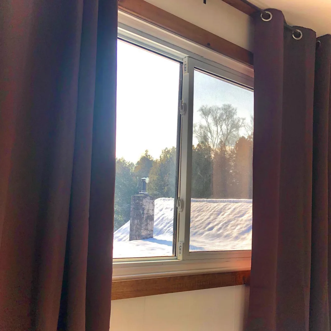 Sunlight through a lodge window onto a snow-covered roof and stone chimney