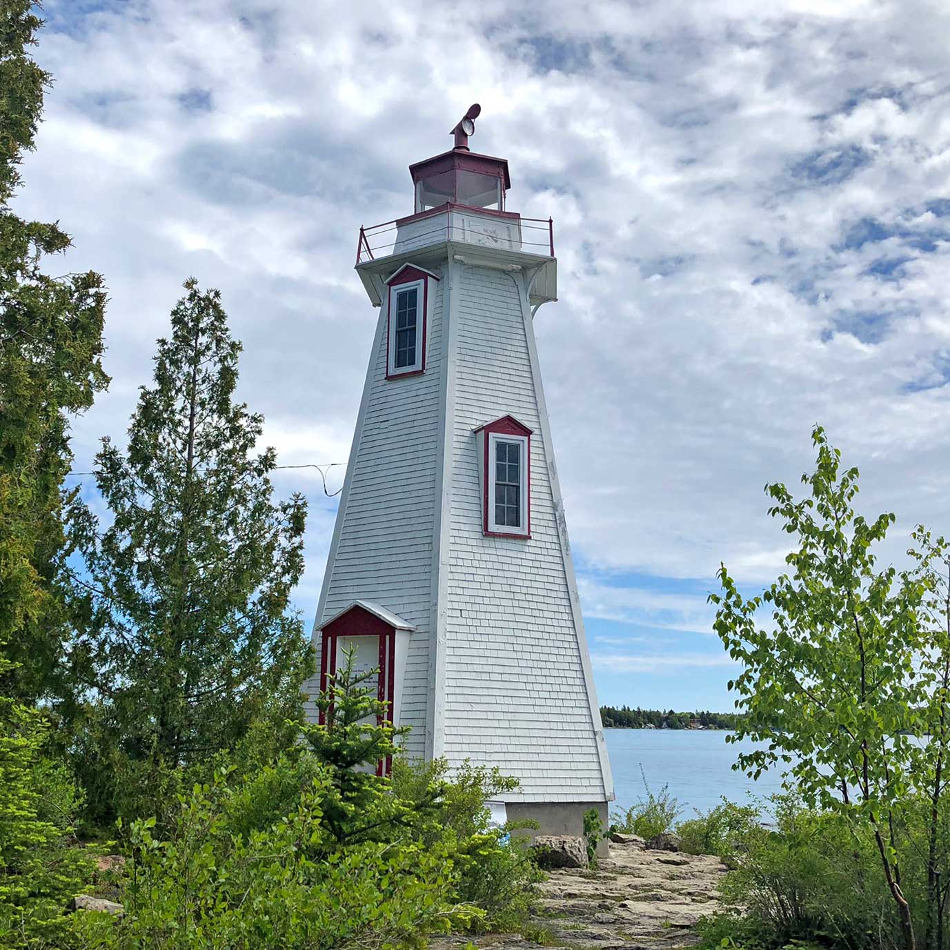 A white wooden lighthouse with red trim among cedars near Tobermory