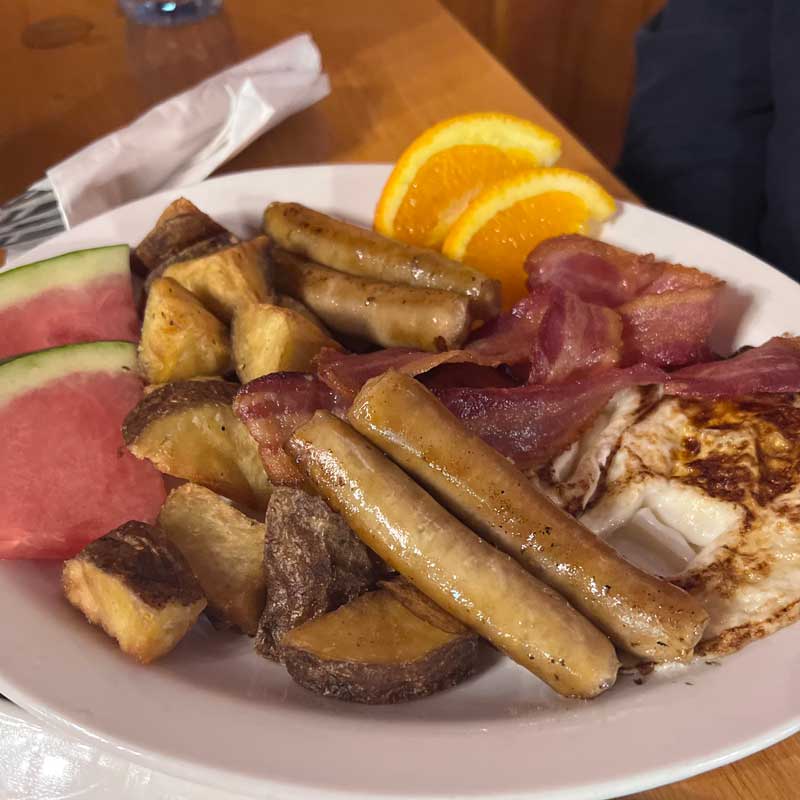 Breakfast plate of sausages, bacon and home fries with an orange slice