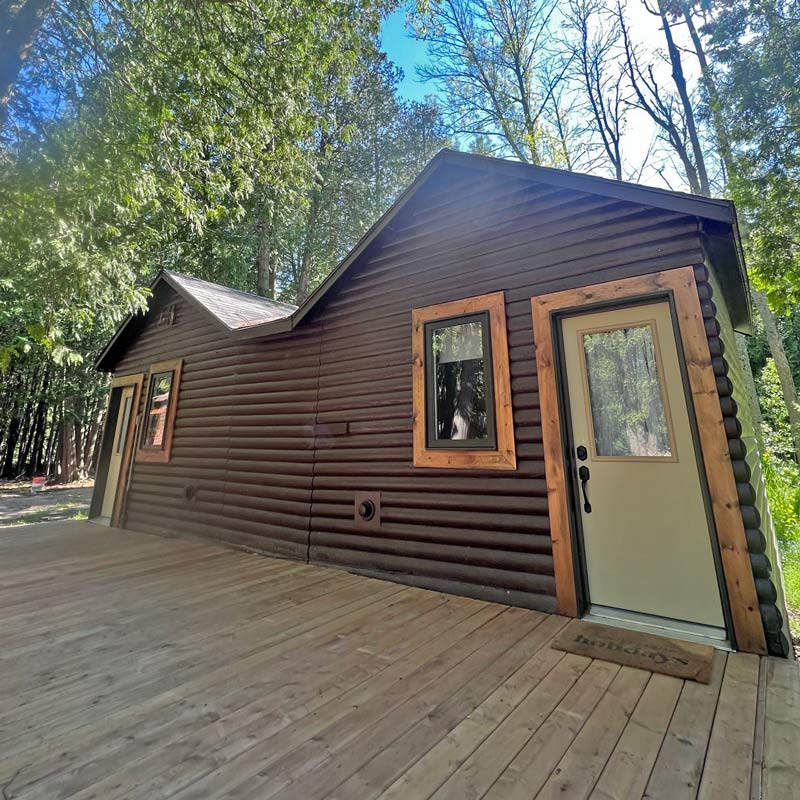 A dark log-sided cabin with a wooden deck, set among cedars at Red Bay Lodge
