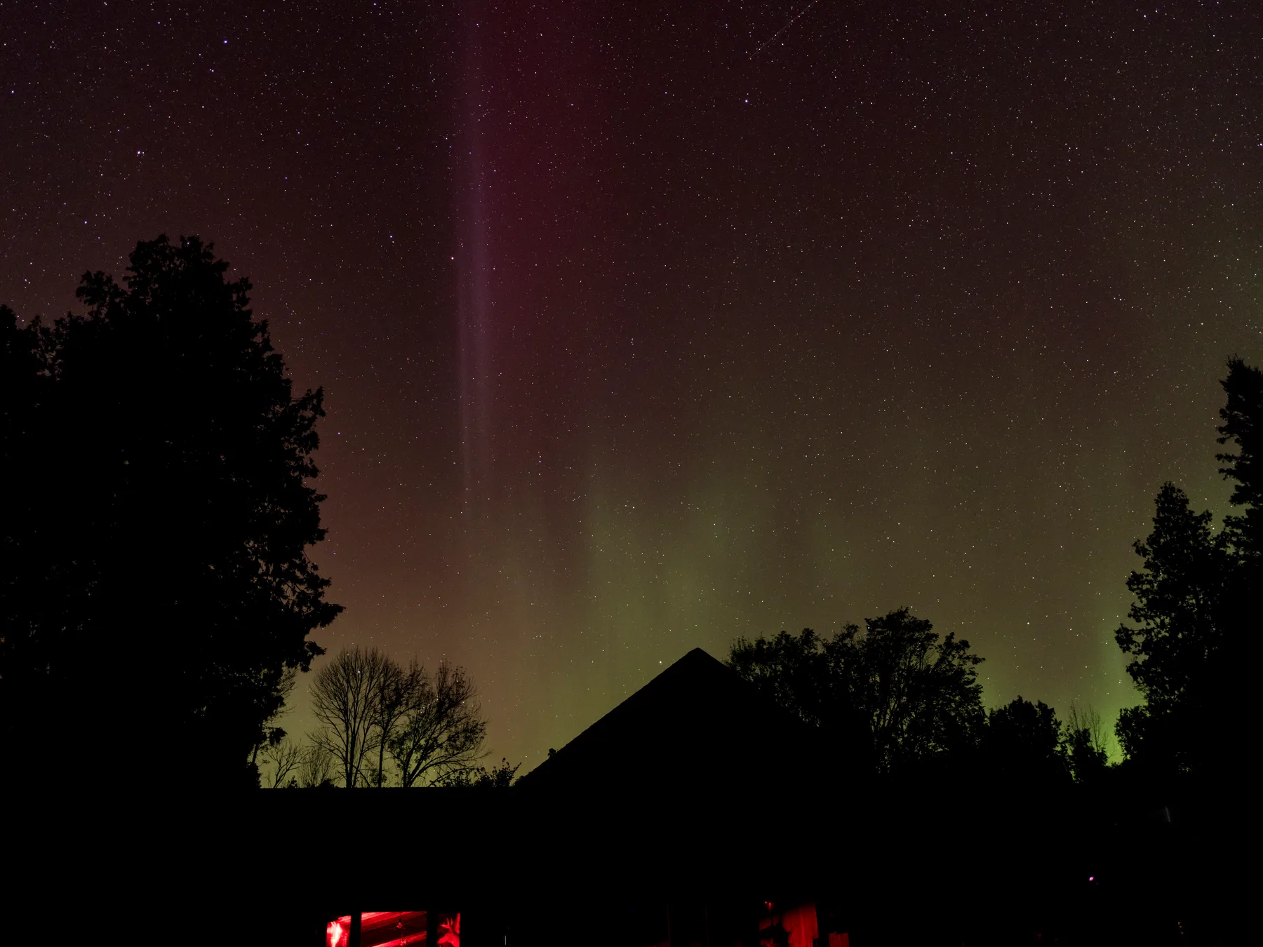 Northern lights over the lodge roof, seen through the trees at night