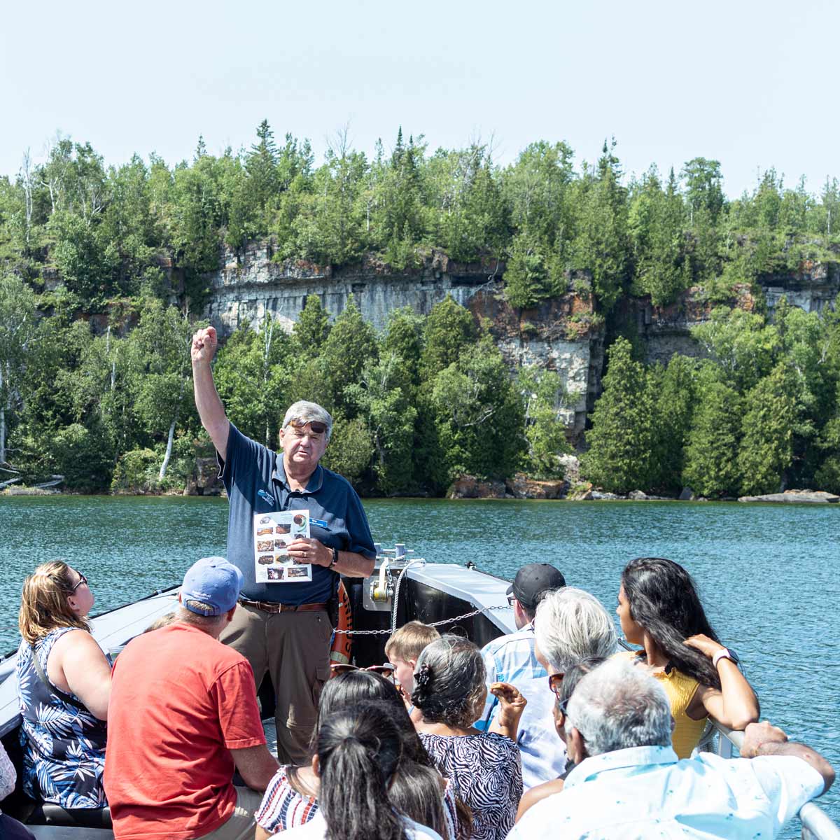 A guide talking to passengers on a boat tour below a limestone cliff